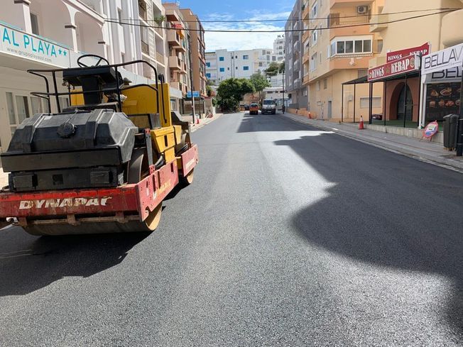 Rodillo compactador de asfalto recién pavimentado en una calle de una zona urbana soleada.