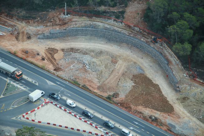 Obra junto a la autopista. Movimiento de tierras, muro de contención y vehículos en la carretera.