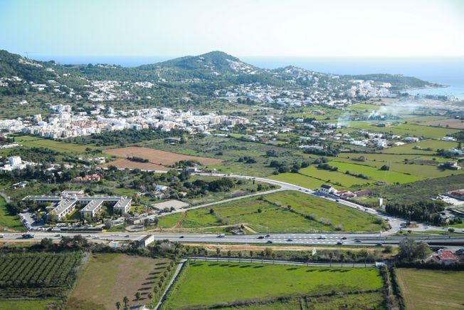 Campos verdes, un pueblo y una autopista se encuentran con el océano bajo un cielo despejado.