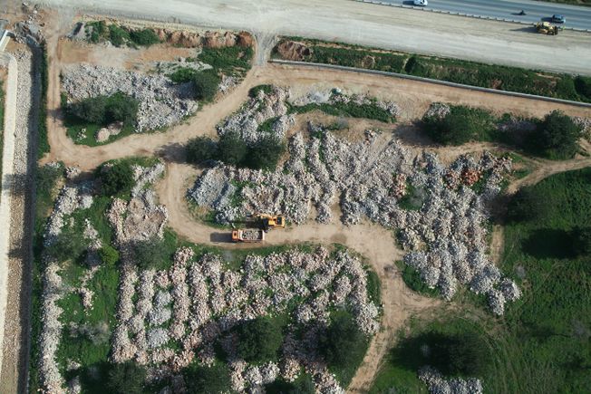 Vista aérea de una obra con montones de escombros, tierra y escasa vegetación. Se ven un camión y una excavadora.