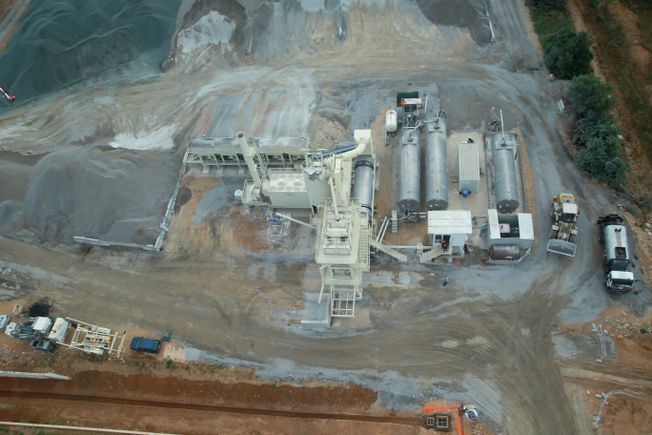 Vista aérea de una planta de procesamiento de grava con maquinaria, silos y camiones en un entorno industrial.