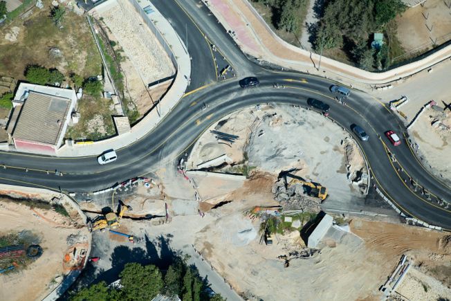 Vista aérea de una rotonda en construcción. Los vehículos circulan por los carriles existentes alrededor de una zona de obras con maquinaria pesada.