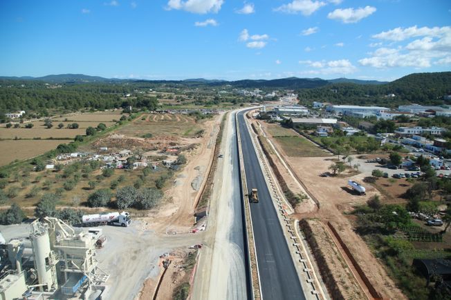 Sitio de construcción de autopista en una zona rural con camino asfaltado y vegetación circundante bajo un cielo azul.