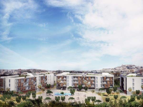 Vista exterior de edificios de apartamentos de baja altura con piscina y árboles bajo un cielo azul, posiblemente un complejo de viviendas.