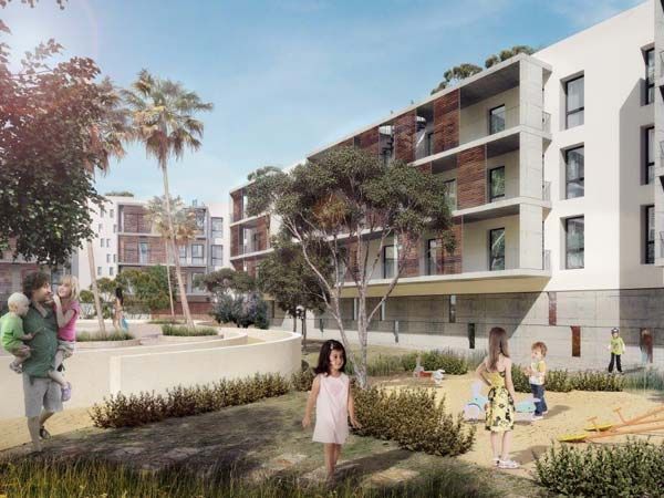Niños juegan en un patio rodeado de edificios de varias plantas. Se ve gente. Día soleado.