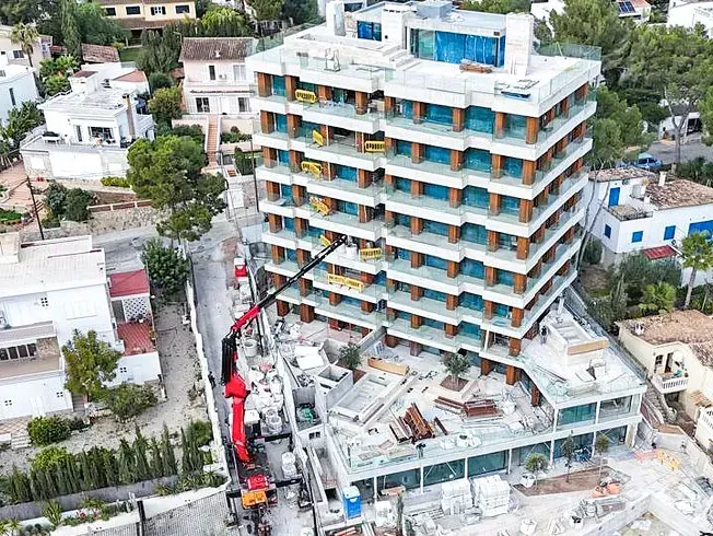 Sitio de construcción: Edificio de varios pisos en construcción, grúa, rodeado de casas y árboles.