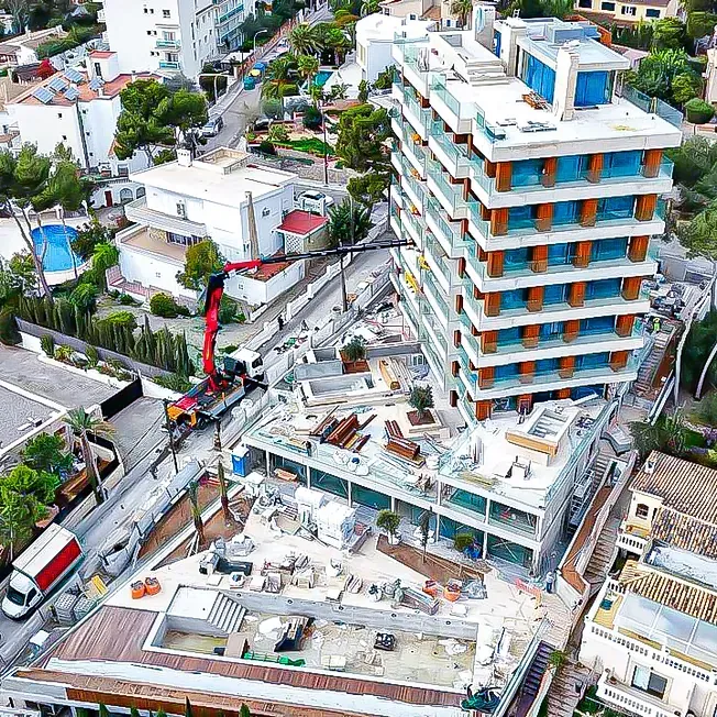 Sitio de construcción con edificio alto y moderno, grúa y casas circundantes.