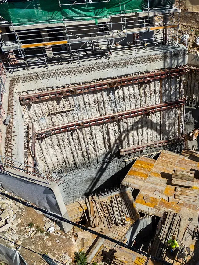 Sitio de construcción con paredes de hormigón y andamios; trabajador visible.