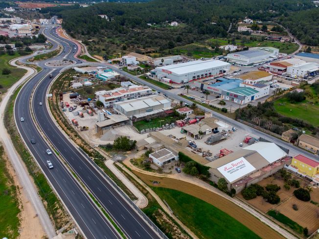 Vista aérea de una carretera de cuatro carriles que atraviesa un paisaje verde cerca de una ciudad costera.