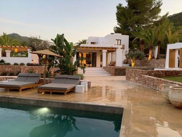 Exterior de una villa de lujo con piscina y tumbonas. Edificio blanco, detalles en piedra y exuberante paisajismo.