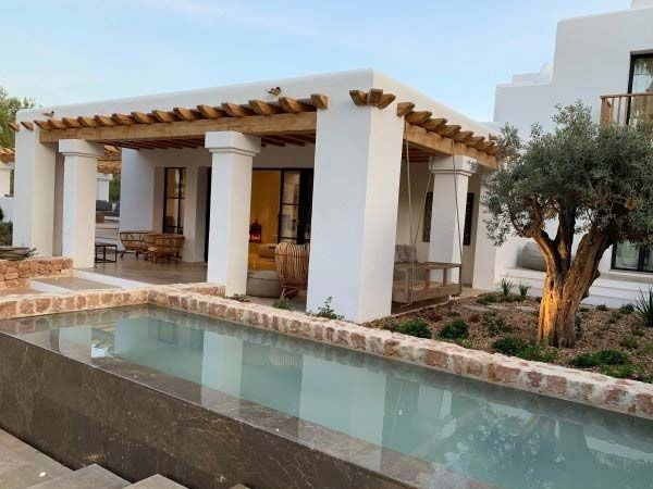 Exterior de una villa de lujo con piscina y tumbonas. Edificio blanco, detalles en piedra y exuberante paisajismo.