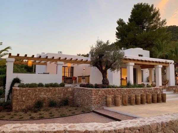Villa blanca con paredes de piedra y vigas de madera, olivo en frente.