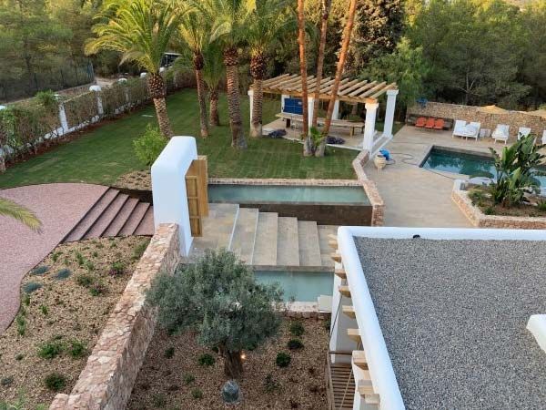 Un espacio exterior sereno con piscina, escaleras y pérgola, rodeado de árboles y exuberante vegetación.