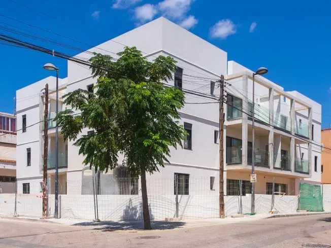 Edificio moderno blanco de varios pisos en construcción con balcones de vidrio, árboles y postes de servicios públicos.
