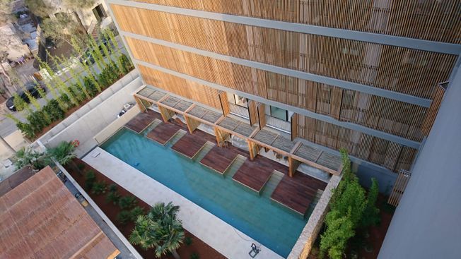 Piscina del hotel con tumbonas, sombrillas de paja y un edificio moderno al fondo.