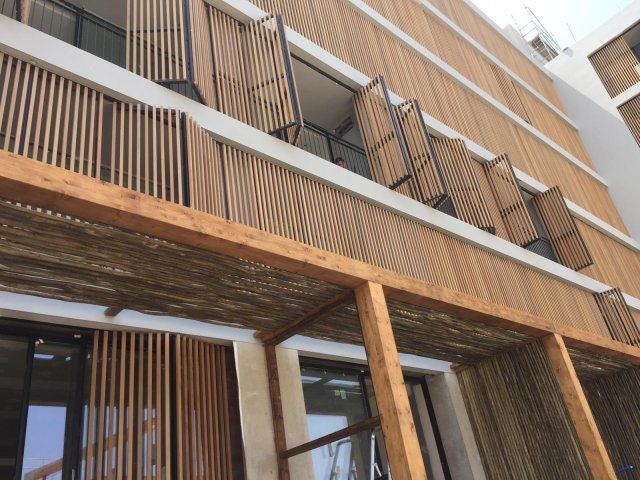 Exterior del edificio con fachada de lamas de madera y persianas abiertas.