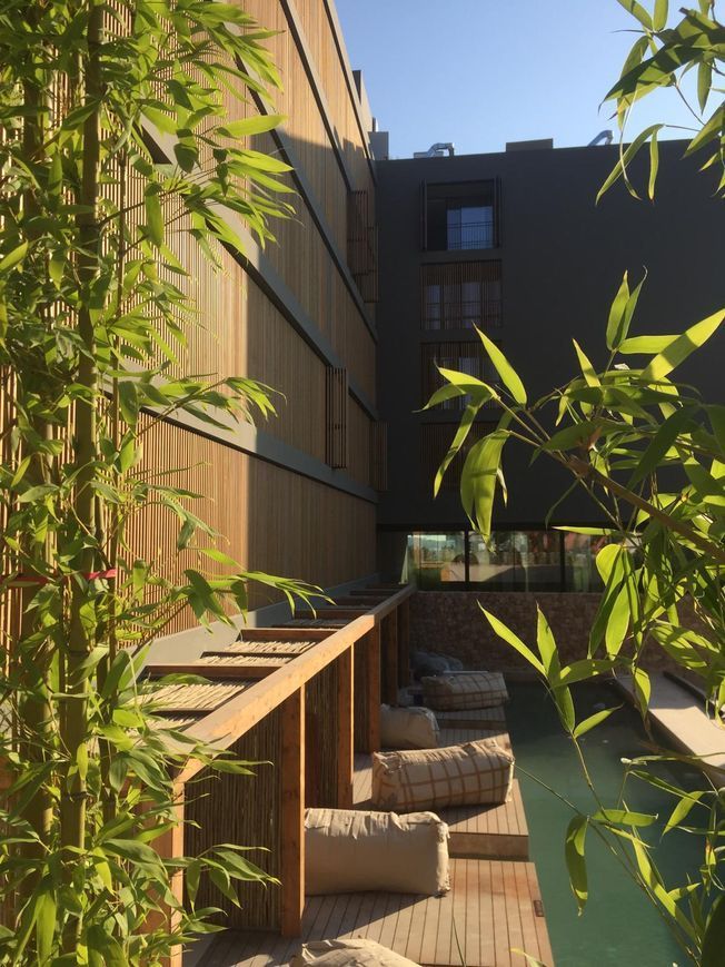 Los marcos de bambú enmarcan una plataforma de madera con cojines cerca de un edificio moderno con revestimiento de madera.