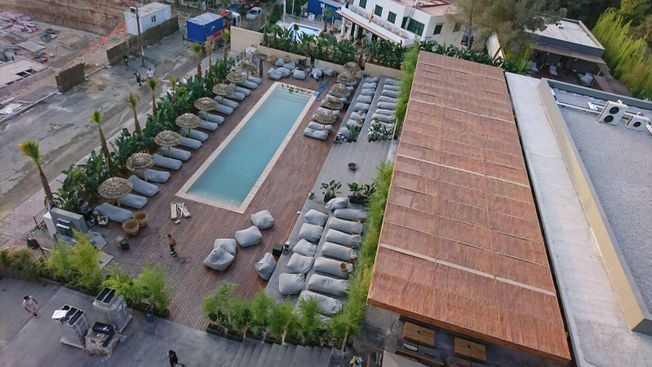 Vista aérea de un área de piscina con tumbonas, pufs y una piscina larga y rectangular.