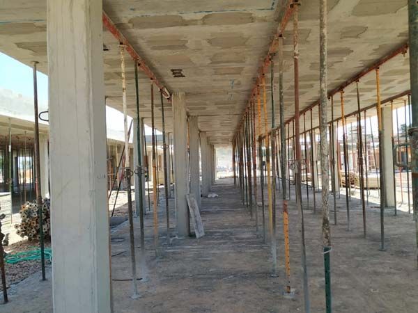 Edificio de hormigón en construcción, sostenido por andamios y columnas metálicas, a lo largo de un pasillo.