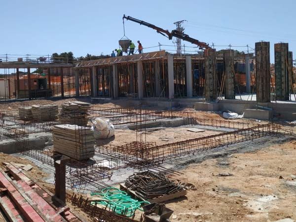 Sitio de construcción con grúa vertiendo hormigón en una estructura de edificio; trabajadores presentes.