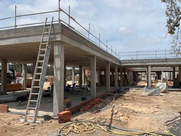 Obra con estructuras de hormigón, árboles y trabajadores. Cielo azul.