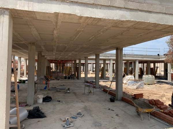 Obra con pilares de hormigón y cubierta de losa. Vista interior con equipos y materiales dispersos.