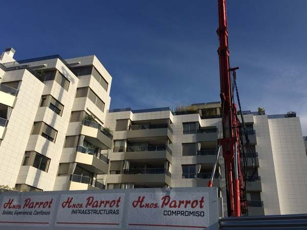 Edificio de apartamentos con balcones, sitio de construcción con grúa roja, cielo azul claro.