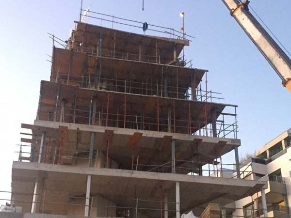 Edificio de apartamentos con balcones, sitio de construcción con grúa roja, cielo azul claro.