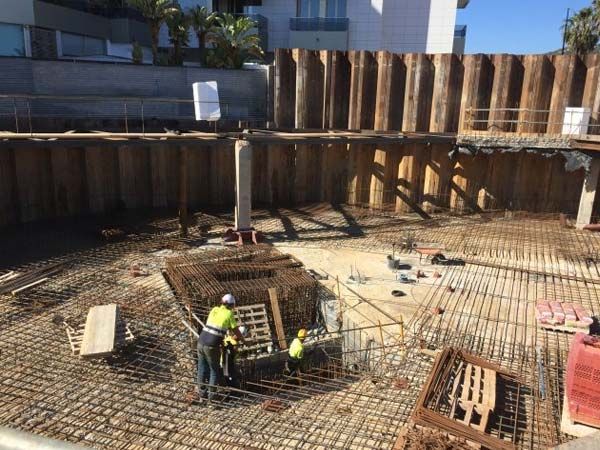 Obra de construcción con obreros, refuerzo de acero, muro de contención de madera.