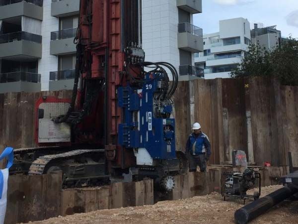 Sitio de construcción con una gran máquina perforadora, un trabajador y un muro de contención de madera.