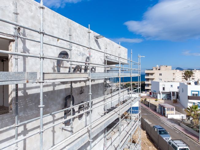 Edificio en construcción con andamios, con vista a la calle y al mar.