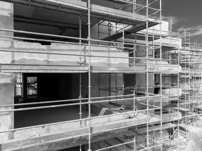 Edificio en construcción, andamio rodeando exterior, blanco y negro.