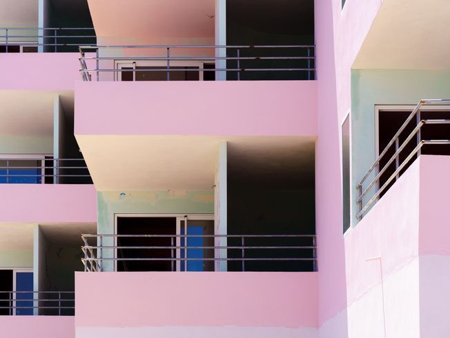 Edificio rosa y blanco con balcones, barandillas de metal y puertas azules.