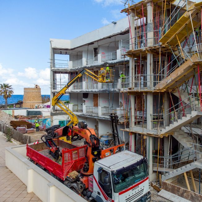 Obra: Obreros en ascensores, quitando paredes de un edificio blanco, camión con grúa al costado.