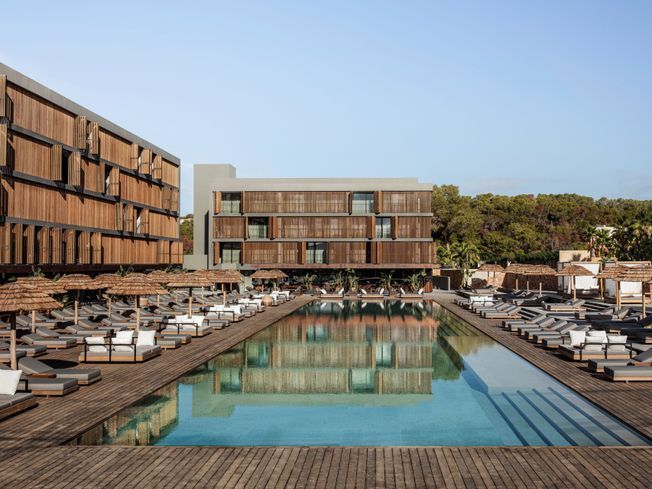 Complejo turístico con edificios de madera, piscina y tumbonas en un día soleado.