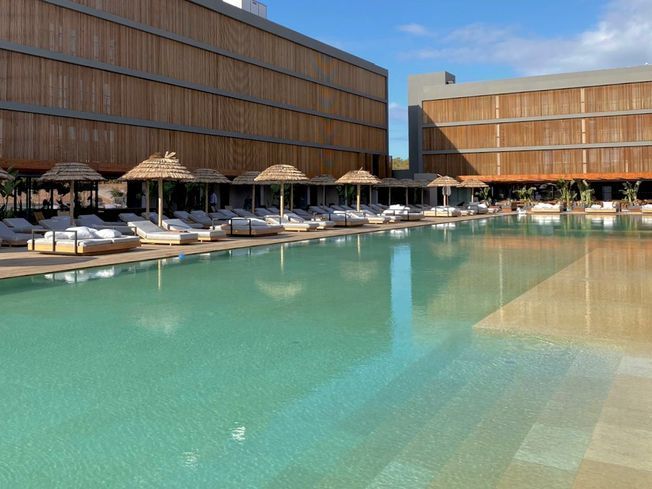 Complejo turístico con edificios de madera, piscina y tumbonas en un día soleado.