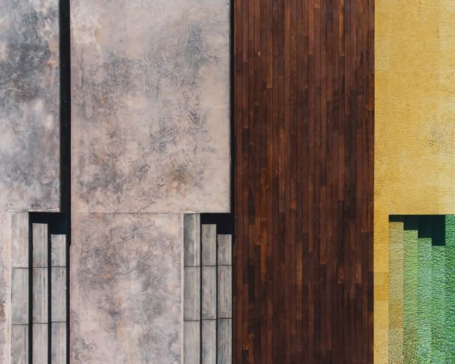 Vista aérea de la fachada del edificio con hormigón, madera oscura y paneles amarillos y verdes.