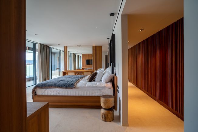 Dormitorio moderno con cama, paredes y mesitas de noche de madera. Incluye amplios ventanales y ropa de cama de lujo.