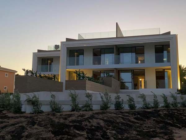 Moderna casa blanca de varios pisos con balcones de vidrio al anochecer, vista frontal.