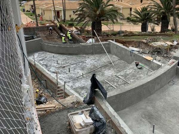 Piscina en construcción con paredes curvas, concreto y obreros.