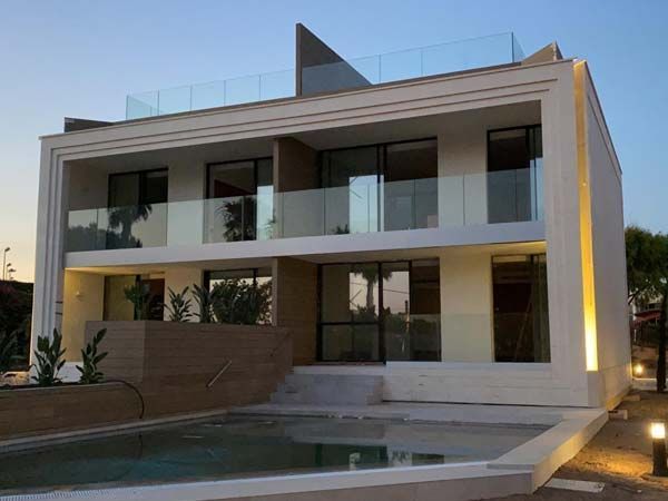 Casa moderna blanca de dos plantas con balcones de cristal y una pequeña piscina. Cielo azul de fondo.