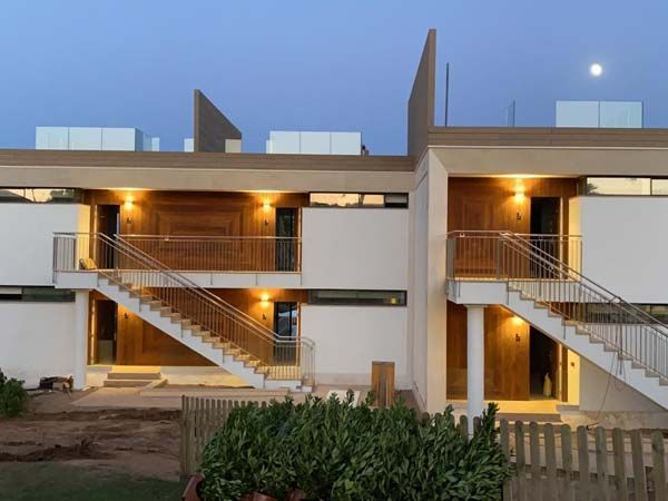 Edificio beige y blanco de dos plantas con escaleras exteriores y puertas iluminadas al anochecer.
