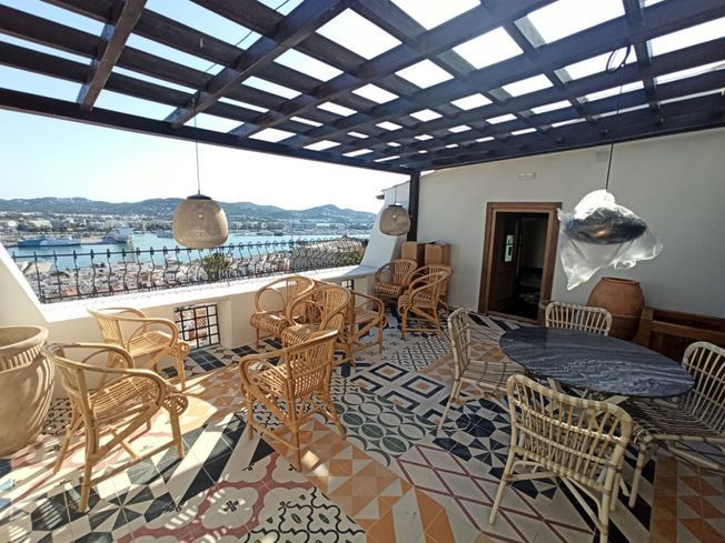 Patio en la azotea con sillas de mimbre, azulejos estampados y vista al puerto bajo una pérgola de madera.