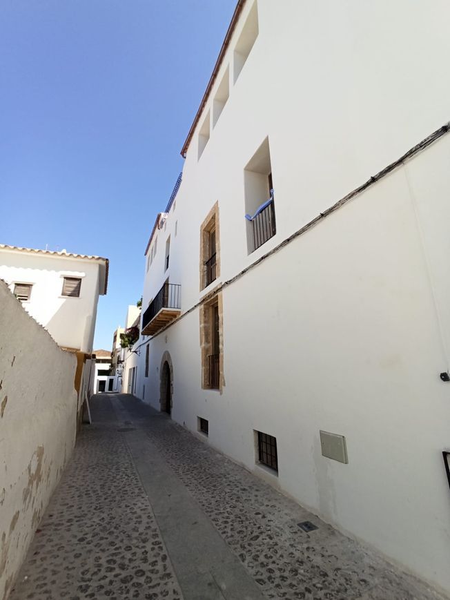 Calle estrecha adoquinada con edificios blancos bajo un cielo azul.