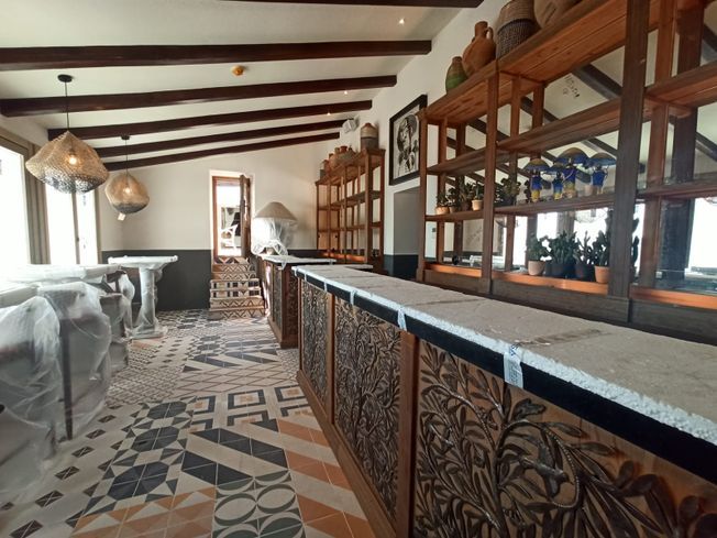 Interior de un restaurante con barra de madera, estantes y suelos de baldosas estampadas.