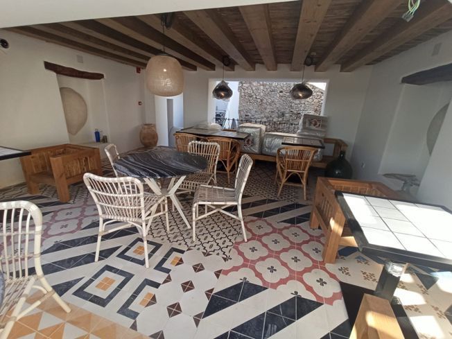 Comedor interior con suelo de baldosas estampadas, mesas de madera, sillas de mimbre y lámparas colgantes.