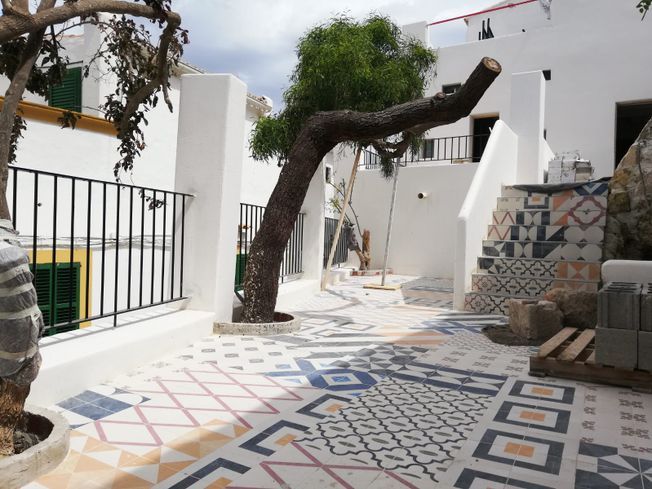 Patio con piso de baldosas estampadas, árbol y edificios blancos.
