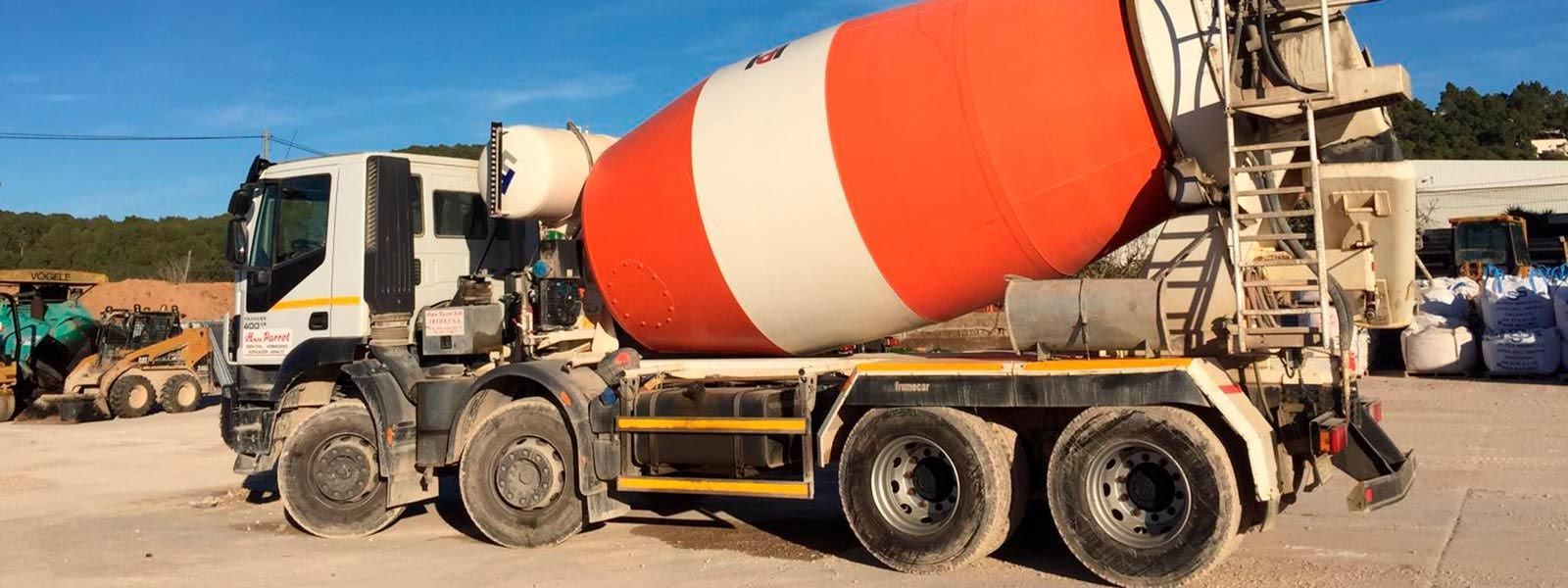 Camión de cemento en un día soleado, con un bidón blanco y naranja. Otros vehículos de construcción al fondo.
