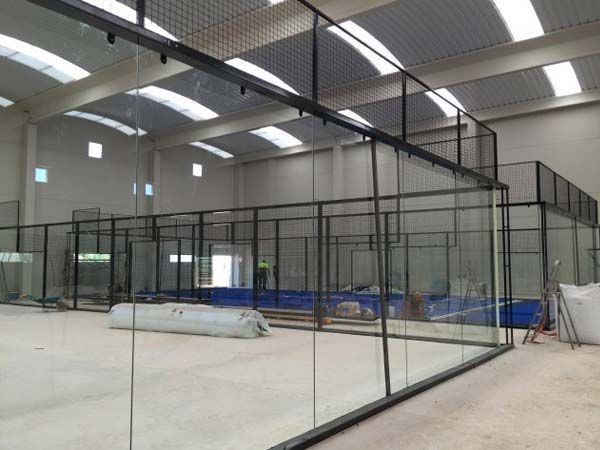 Pista de pádel cubierta con paredes de cristal y estructura metálica de color negro.