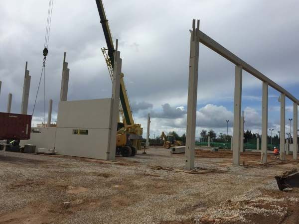 Sitio de construcción: Grúa levantando vigas de hormigón para la estructura de un edificio; cielo nublado, suelo de grava.
